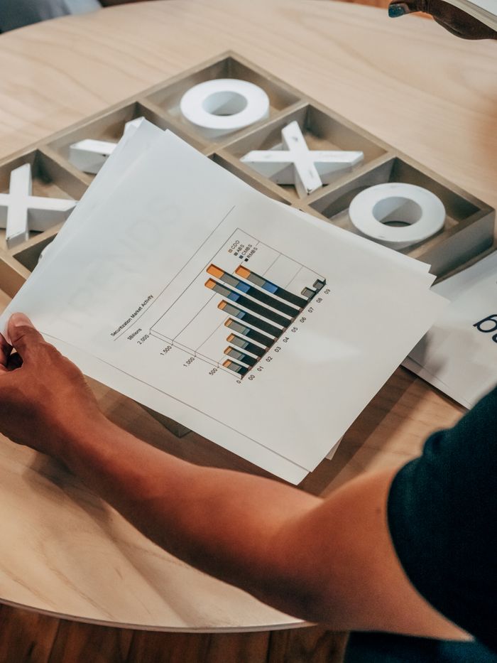 Gros plan sur une main tenant un document d’analyse commerciale avec des graphiques, posé sur une table en bois à l’intérieur.