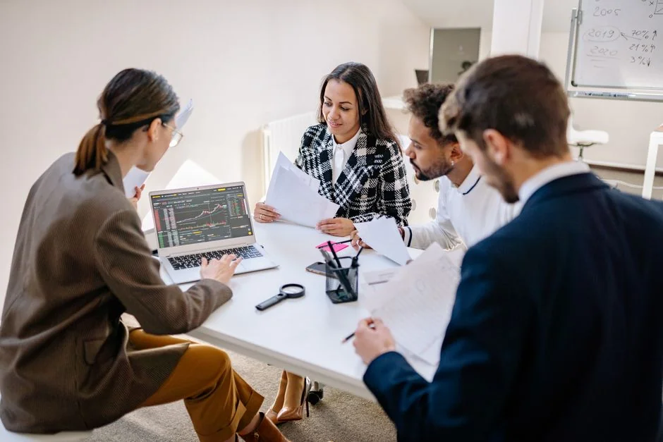 A contemporary workspace where hands review marketing data on a laptop alongside printed documents.